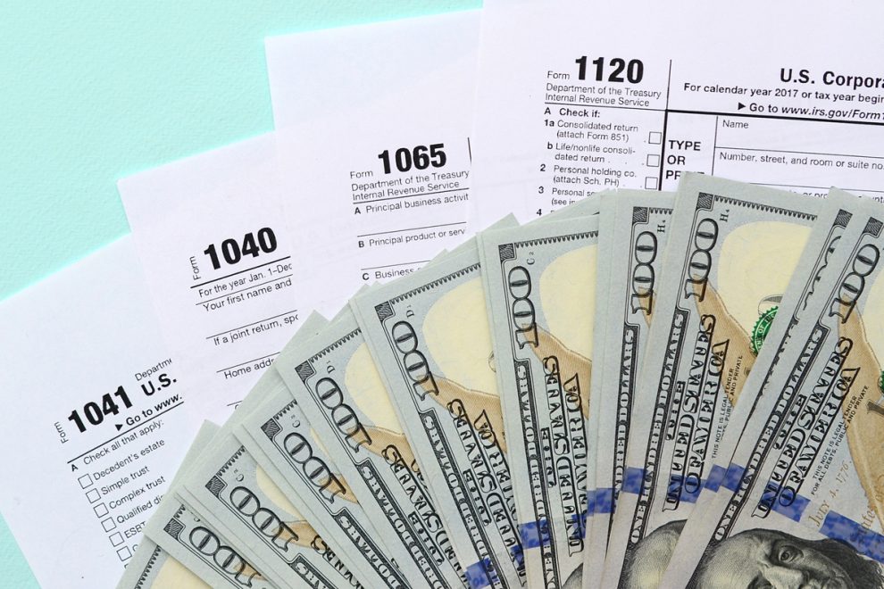 Tax forms lies near hundred dollar bills and blue pen on a light blue background. Income tax return