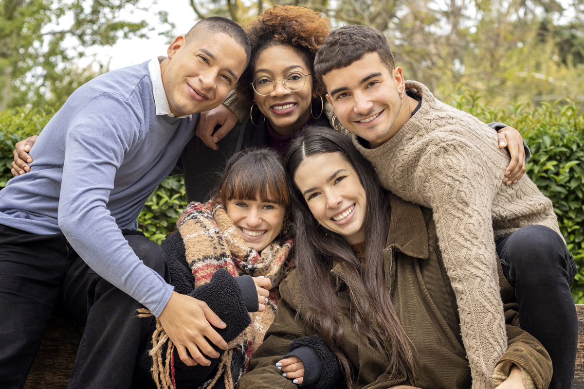 group of five young friends sitting on a park bench happy and sm