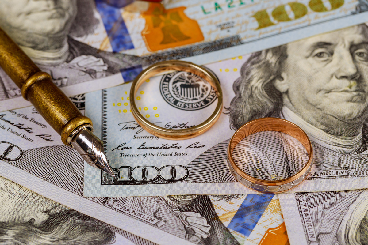 Marriage contract of convenience, wedding ring on pen on dollar banknotes background