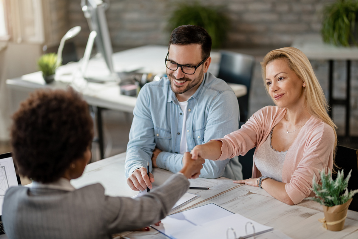 Happy couple handshaking with insurance agent while meeting in t