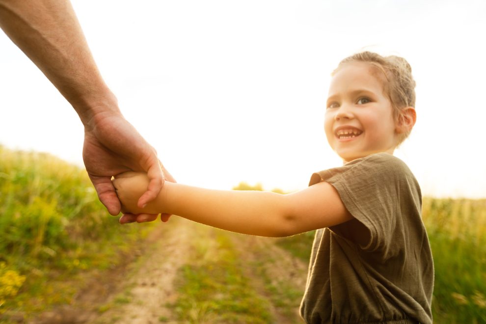 Little girl holding her dad’s hand and looking back